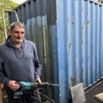 Volunteer with a saw in front of a blue shipping container for Slice of Hope