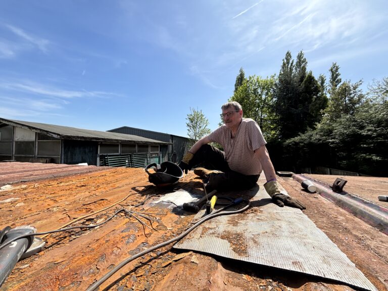 Volunteer with welding kit working on a metal roof during the Slice of Hope build