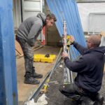 People using a laser level between shipping containers on the Slice of Hope build