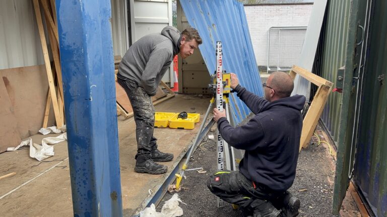 People using a laser level between shipping containers on the Slice of Hope build